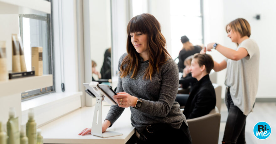 A lady busy on a tablet with people getting their hair cut in a hair salon